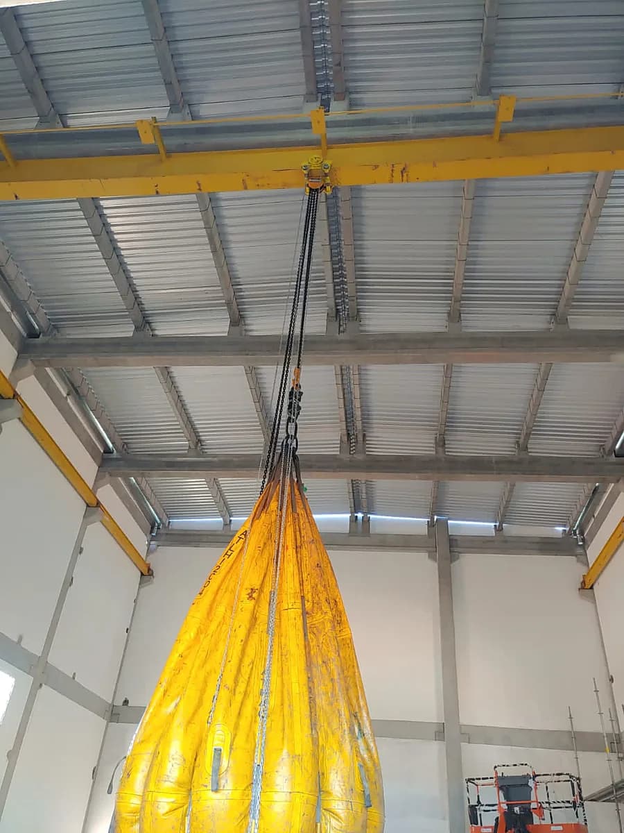 Ensaio de carga com bolsa d'água amarela suspensa por talha manual de baixa altura em viga de galpão
